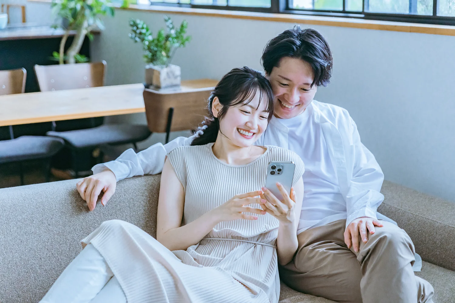 ソファでスマートフォンを笑顔で見るカップル