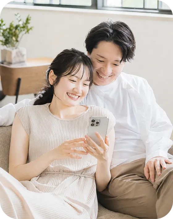 ソファでスマートフォンを笑顔で見るカップル